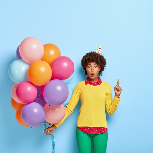 wondered woman holds multicolored balloons while posing yellow sweater